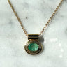 A gold chain necklace with a round bezel-set green gemstone pendant, displayed on a white marble surface.