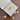 Gold-tone jewelry set with a necklace and three matching earrings displayed on a beige jewelry box, placed on a wooden surface. The flower-shaped pendants feature red, green, and clear stones in the center.